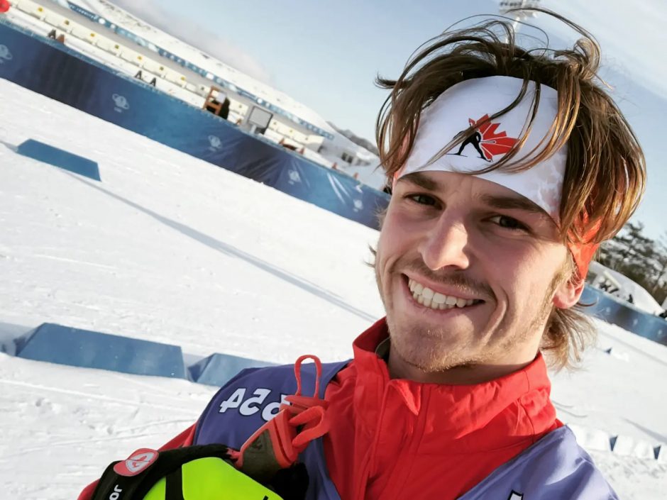 Smiling white man in 20s wearing ski gear and Team Canada headband at a ski track